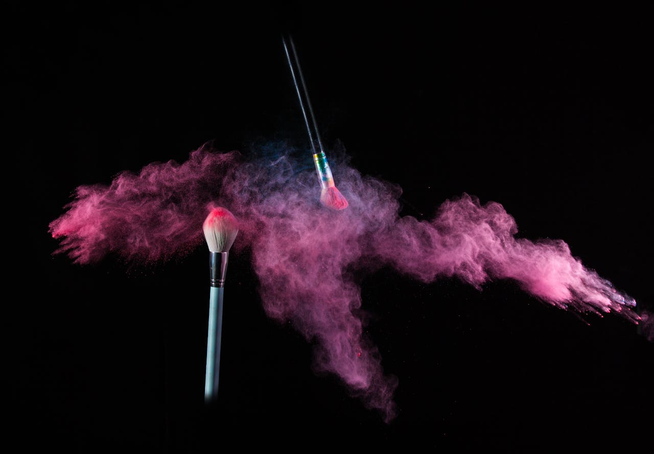 Crafting Captivating Headlines: Your awesome post title goes here Two makeup brushes dynamically releasing pink powder against a black background.